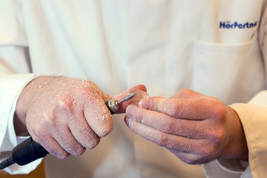 Ein Hörakustiker schleift individuell ein Hörgerät für eine optimale Hörgeräteanpassung.